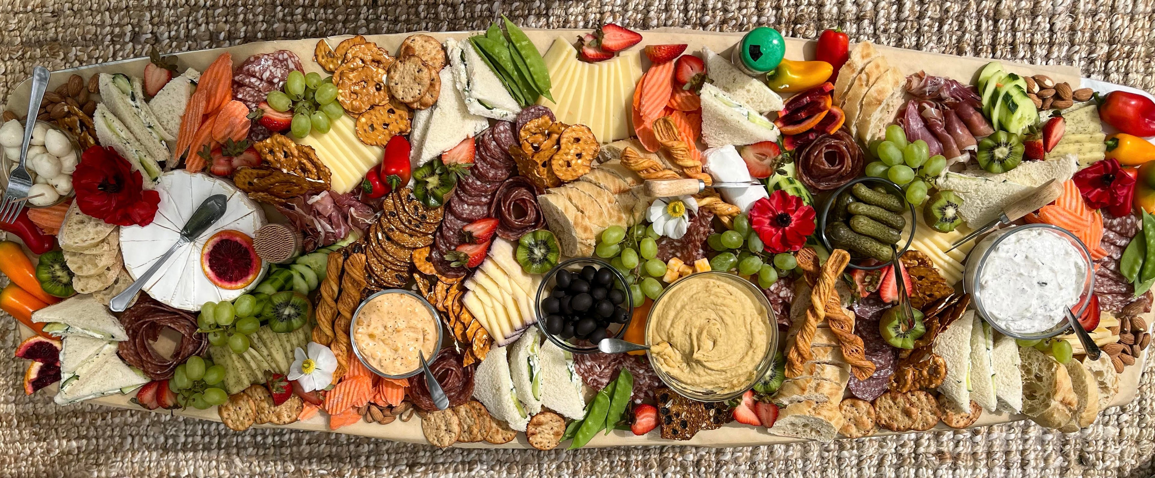 A luxury cheese and charcuterie grazing table containing a wide assortment of cheese, charcuterie, crackers, dips, olive, pickles, and more! This beautifully styled display is a flat lay style spread.