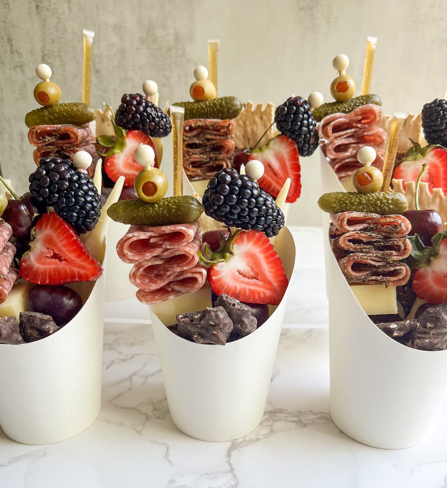 These individual serving charcuterie cups are perfect for the next office gathering, team event, customer appreciation gift, or wedding cocktail hour! Individually packaged for easy grab-and-go. Each includes: gourmet cheeses, artisanal salami, crackers, fresh and dried fruit, nuts, honey stick, various accompaniments (i.e., olives, cornichons, chocolate, etc.) Available for Sacramento event catering and delivery. 