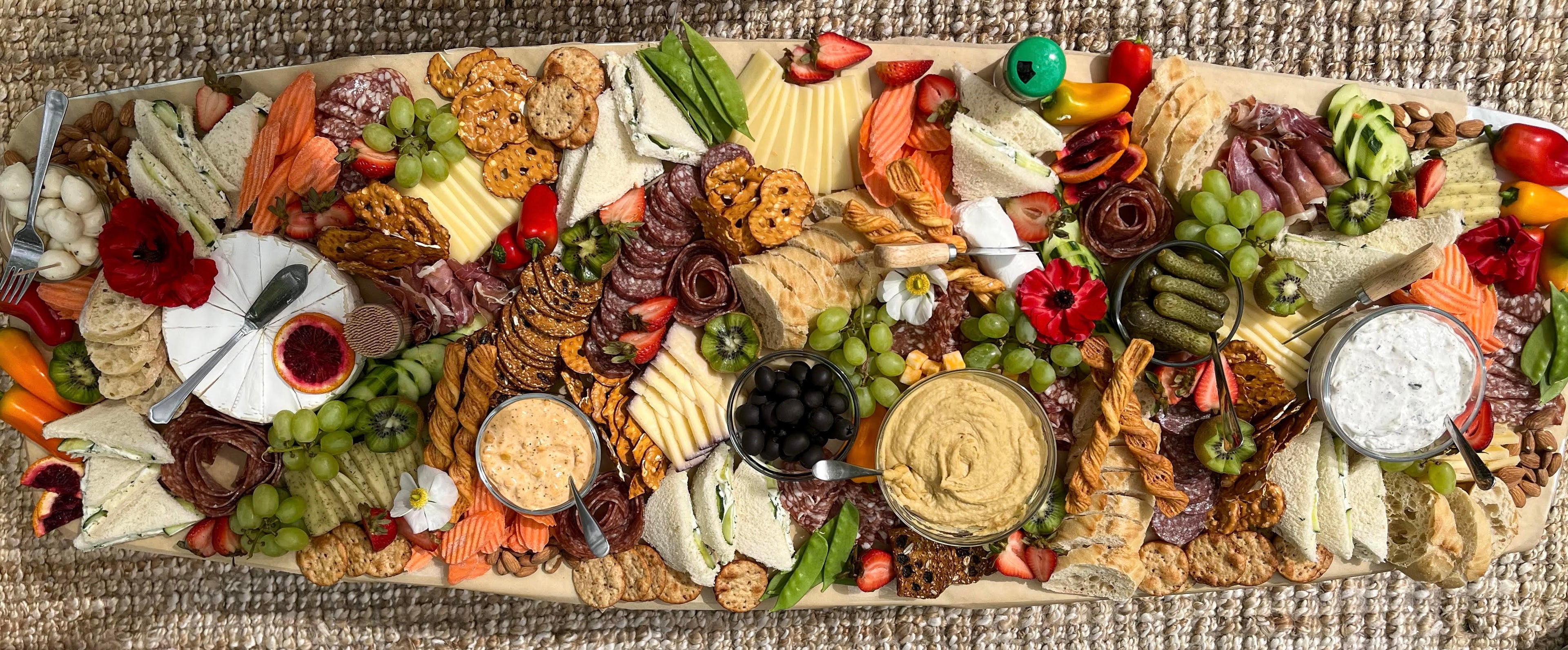 A luxury cheese and charcuterie grazing table containing a wide assortment of cheese, charcuterie, crackers, dips, olive, pickles, and more! This beautifully styled display is a flat lay style spread.  